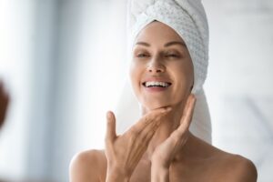 Woman feeling her skin whilst smiling in the mirror
