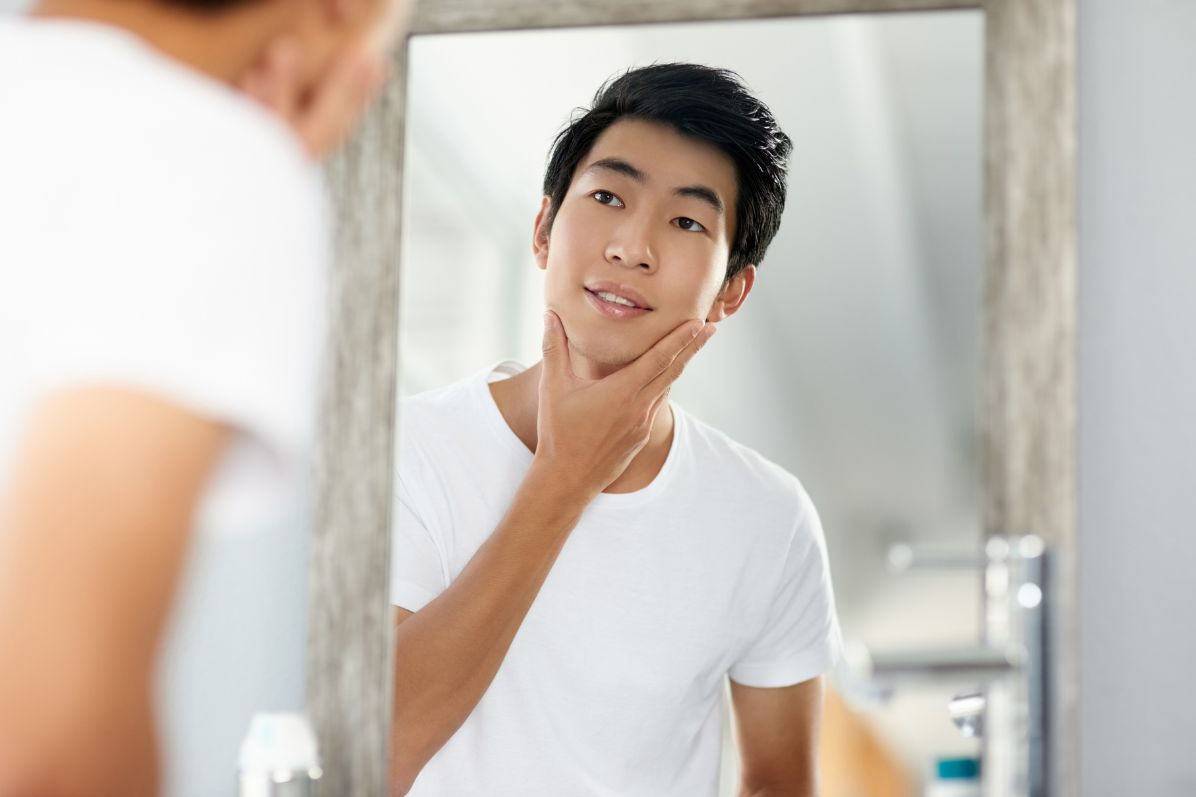 Man looking at his smooth skin in mirror after a HyrdaFacial