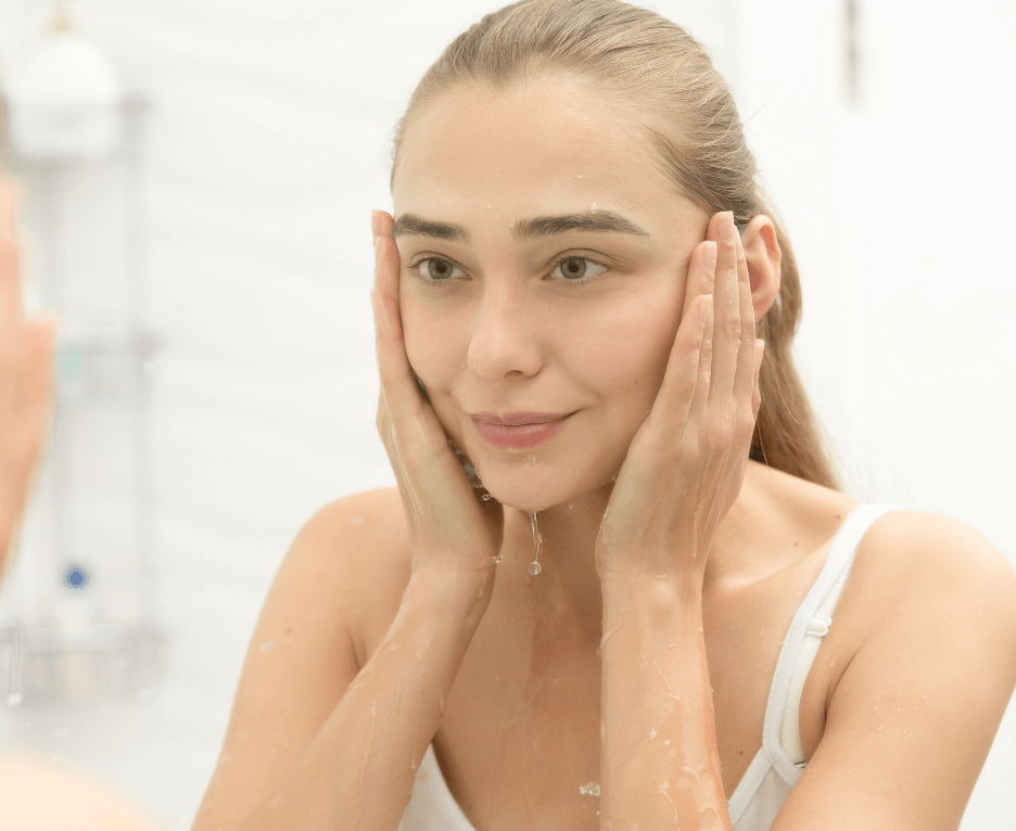 woman looking at herself in the mirror whilst splashing her face with water