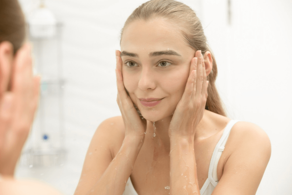 woman splashing her face with water whilst looking in the mirror